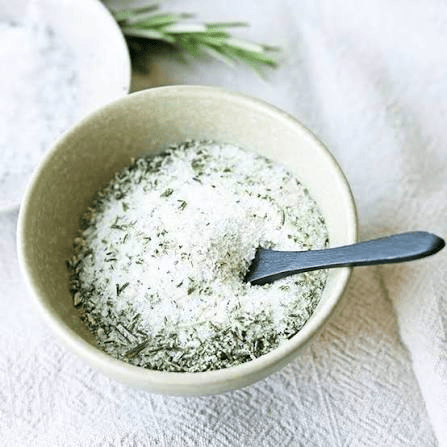 coarse salt flecked with finely chopped green herbs spread on a white plate to dry.