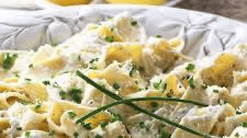 Close-up of creamy noodles garnished with chopped chives and black pepper in a white patterned bowl.