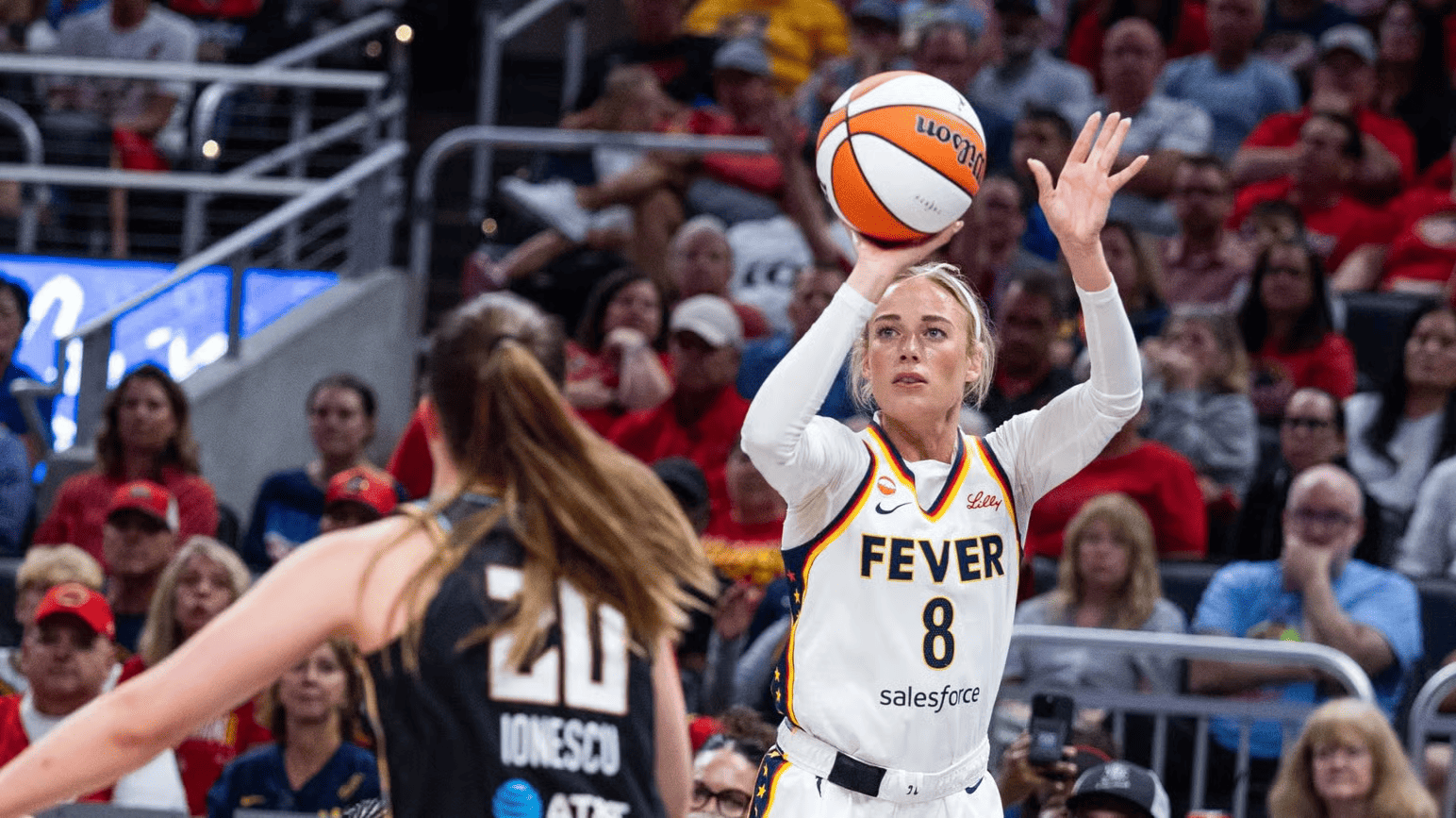 Indiana Fever player No. 8 rises to shoot a basketball over a defender in a black jersey labeled “20 IONESCU” during a packed arena game. Her jersey reads “FEVER” and “salesforce,” with a “Lilly” sponsor patch.