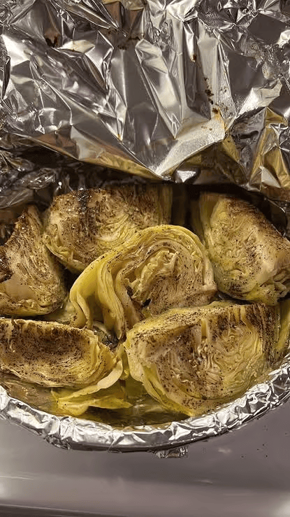 Foil-lined dish filled with seasoned artichoke halves or quarters, roasted until browned and tender, with crinkled aluminum foil covering the top.
